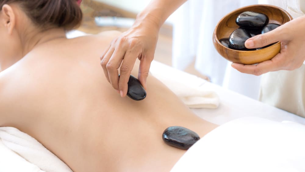 In a spa salon, a woman receives a back stone therapy massage.
