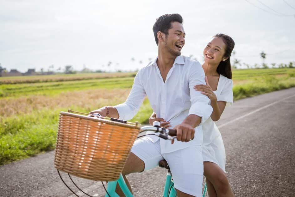 A woman and her lover enjoy riding their bicycles outside in a white clothing.
