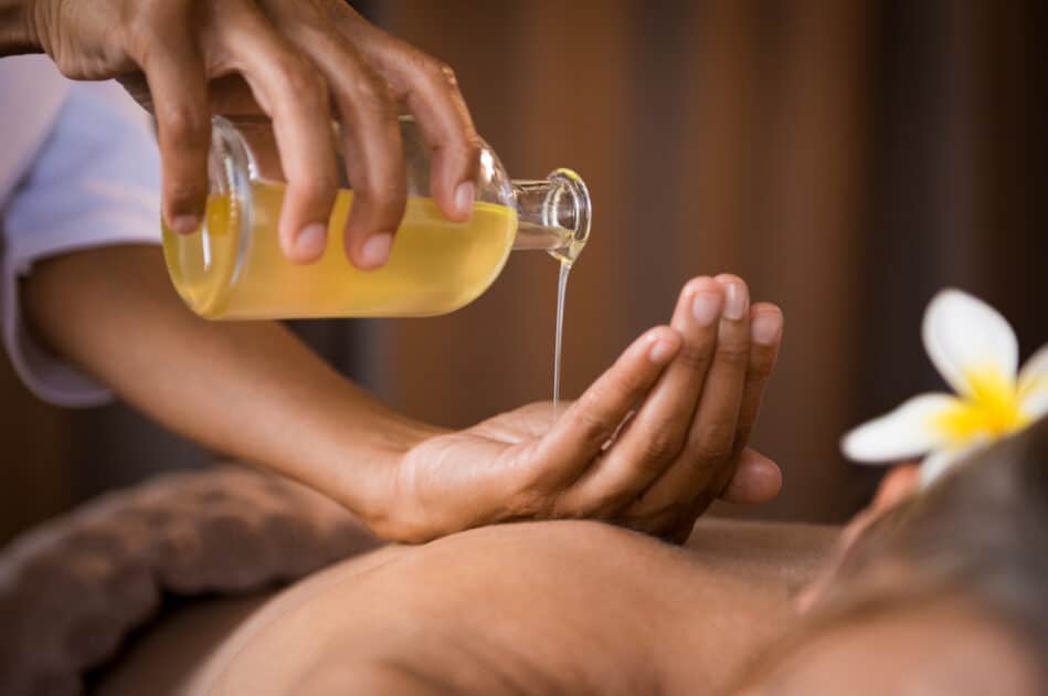 View of the hands of a masseuse applying fragrance oil on a woman's back.