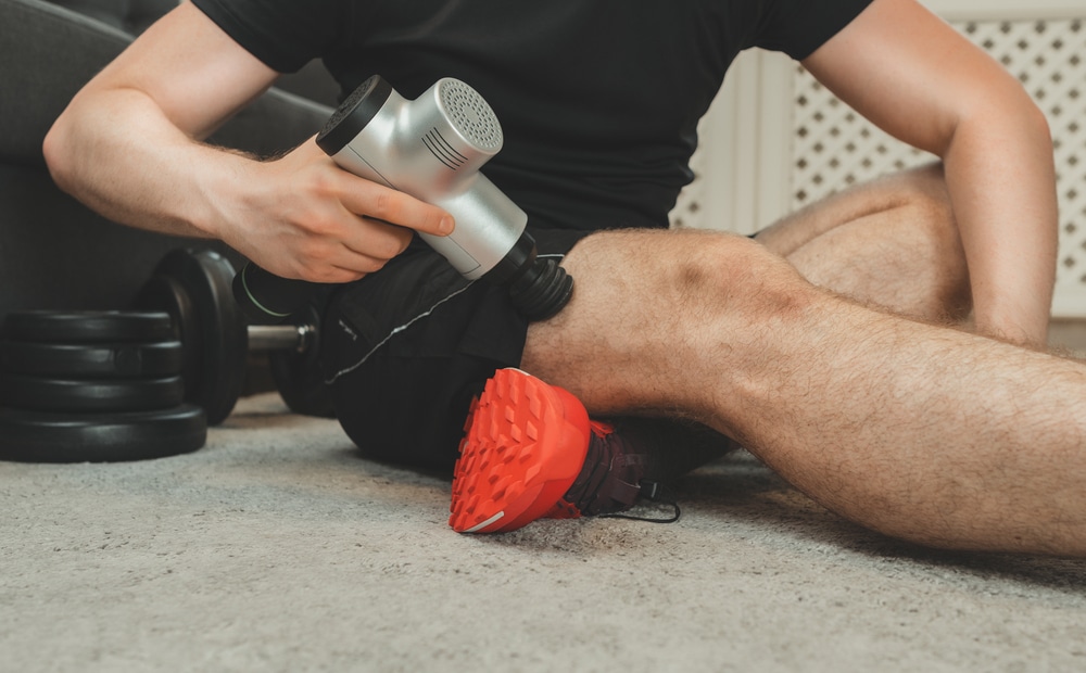 A man uses a percussion massage gadget to massage his leg.


