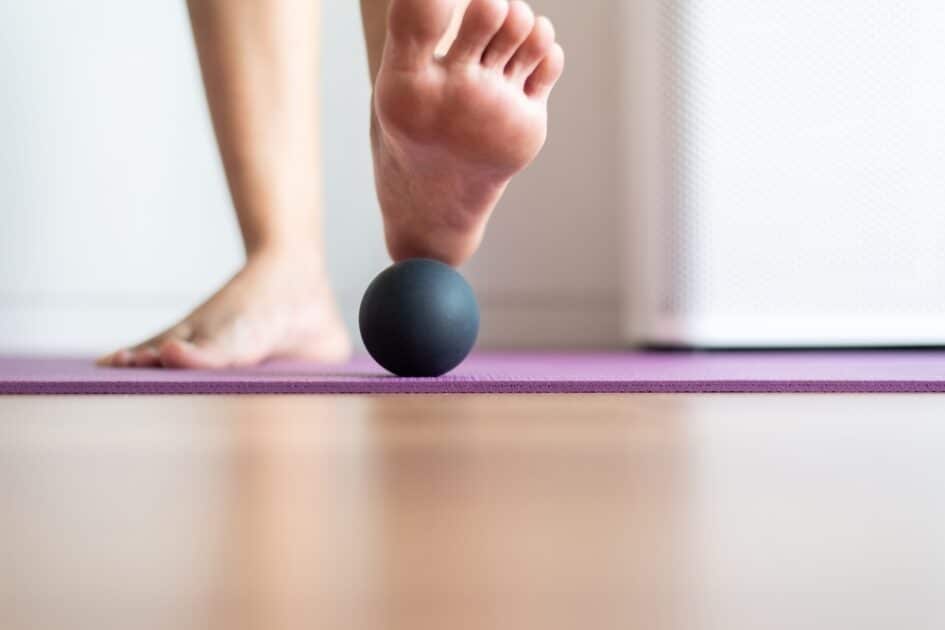 Woman massaging her feet with a rubber ball, foot sole massage for plantar fasciitis