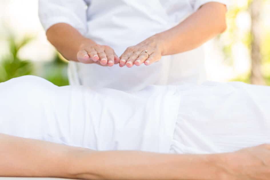 cropped image of a man undergoing reiki therapy while resting on a massage table.