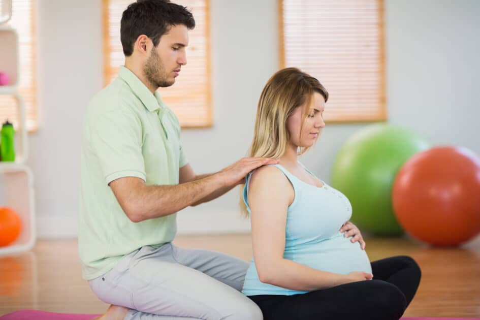 In a studio, a masseuse gives a pregnant woman's shoulders a massage.